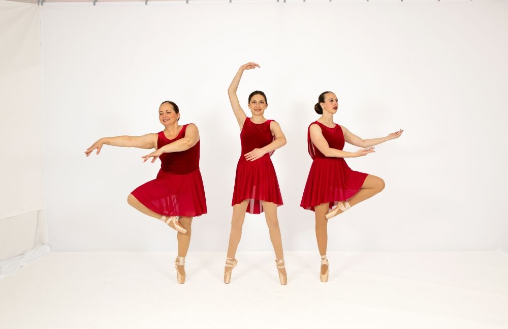Three dancers in red costumes in arabesque